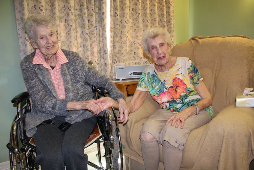Sitting in a room in Seaview Manor in Glace Bay, Ida Macdonald, left, holds Marguerite Caldwell’s hand, concerned her friend might be cold. The women are turning 100 this month and have many stories of bonfires in Round Island, Knox United Church dances in Glace Bay, bowling and golfing.
