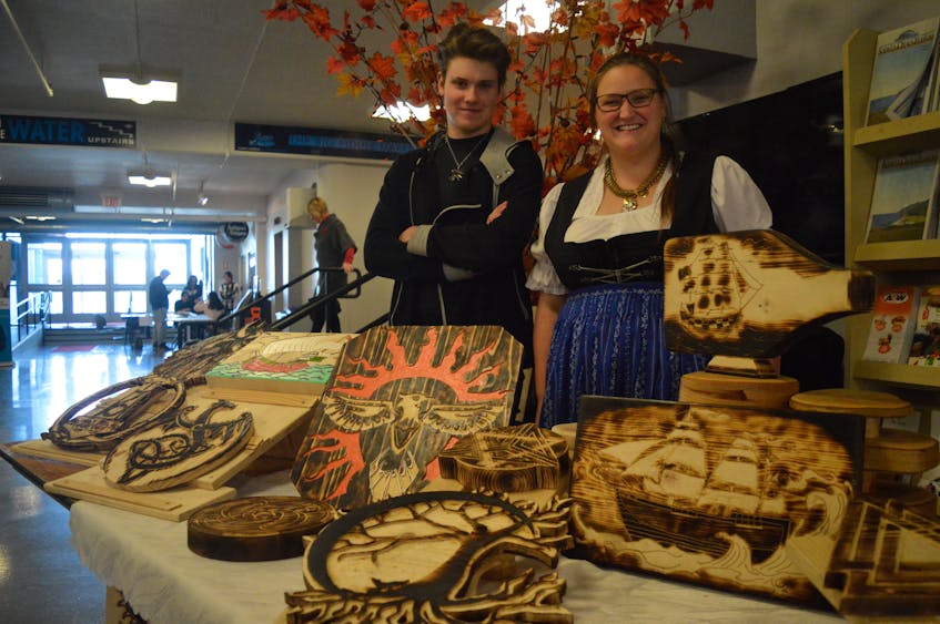 Toni Bruederich, 19, and his sister Lisa Bruederich, 29, stand behind the display showcasing his artwork at the Hello Cape Breton multicultural festival on Sunday at the Joan Harriss Cruise Pavilion. The siblings immigrated to Canada from Germany with their family two and a half years ago and Toni said he started doing the burned wood carvings to get through the long Cape Breton winters.