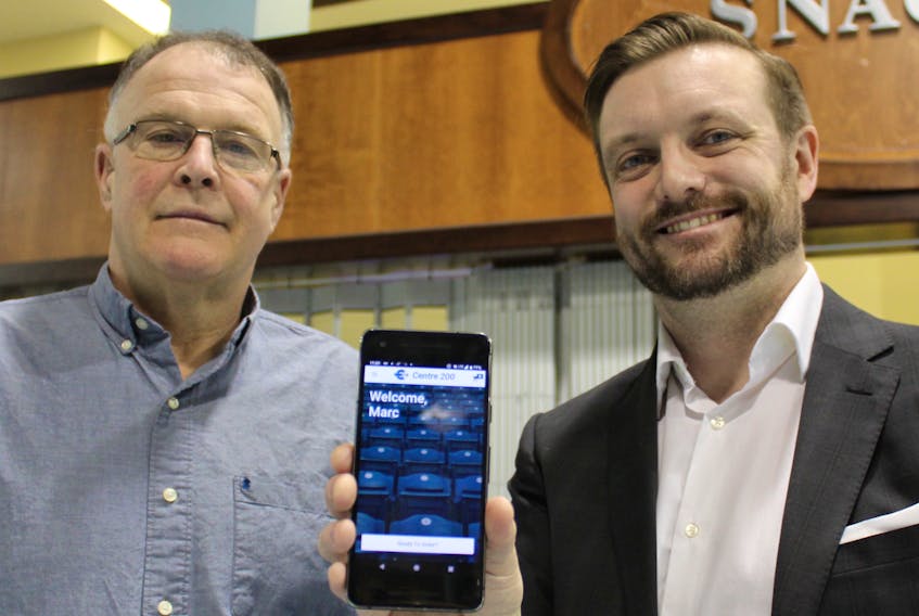 Marc Botte, right, chief marketing officer of 902 Advertising Group, holds his phone displaying the new Centre 200 app, which will allow patrons to order canteen food for in-seat delivery during sporting events and concerts. Centre 200 general manager Paul MacDonald, left, said the pilot project will offer convenience for fans who don’t want to miss a minute of the action.