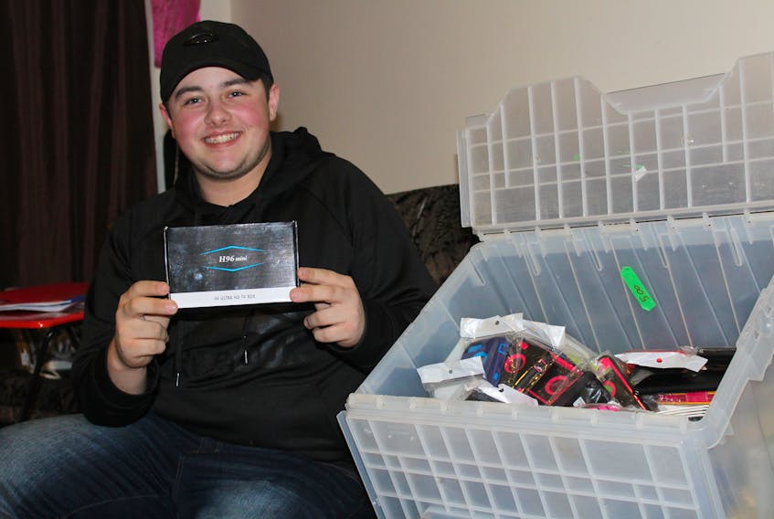 Jayden Green, 16, sits in the living room of his Glace Bay home holding one of the android boxes he is selling through his business JayG Electronics. Beside him is a box of cell phone cases and accessories, Green’s second biggest seller next to the boxes which he sells online and locally.