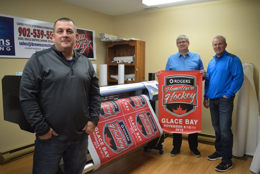 Glace Bay is gearing up for the Rogers Hometown Hockey festival this weekend by painting the town red with decorations and banners like these see-through vinyl window stickers being printed off at Brown’s Cresting in Sydney. Organizers are also printing off a 40-foot banner to be put across Reserve Street and smaller banners, like the one David MacKeigan (centre) is holding. With MacKeigan, from left, are Shawn Brown and Dwight Brown, owners of Brown’s Cresting.
