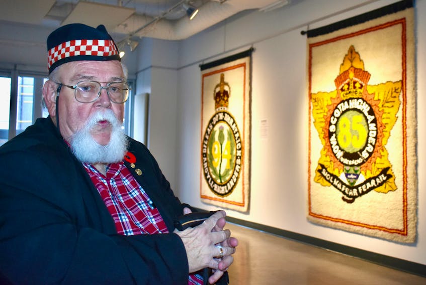Leonard Boudreau of Sydney, former battalion adjutant of 2nd Battalion Nova Scotia Highlanders (CB), takes a moment to reflect while his tapestries depicting the hat badges of local infantry battalions hang in the background at the Cape Breton Centre for Craft and Design in downtown Sydney.