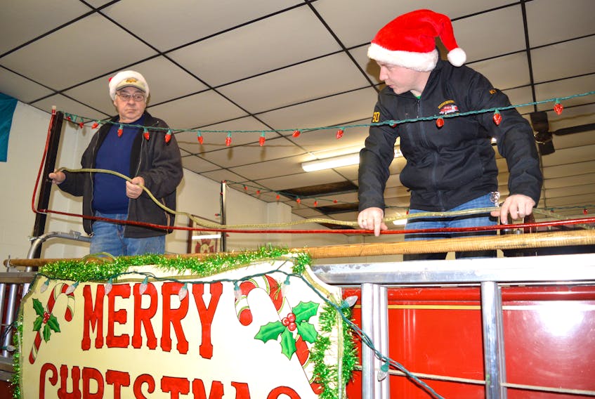 Harold Williamson (left), a 48-year member of the Scotchtown Volunteer Fire Department who retired from his position of fire chief last year after 20 years, and Kyle MacLeod, firefighter, put up some lights on one of the fire trucks in preparation for taking Santa Claus around their coverage area Dec. 18-19. Williamson said this has been a tradition of their department for 64 years now.