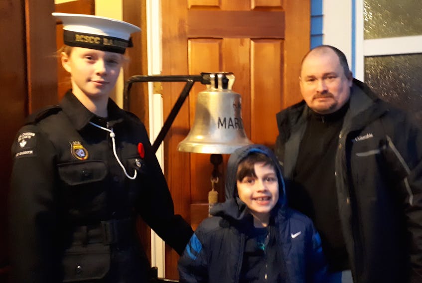 Cadet Katelyn Norman, 12, of Baddeck and eight-year-old Skyler Dawson of Englishtown prepare to ring the bell with Rev. Brian MacLeod at Knox Presbyterian Church in Baddeck on Remembrance Day.