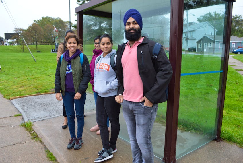 Cape Breton University students, from the left, Harleen Kaur, Ekam Dhingra and Gobindpreet Singh, originally from India and now living Sydney, wait for a Transit Cape Breton bus at a bus stop in Sydney, Tuesday. Singh said on Monday he had to wait more than an hour and let four buses pass him by, to find one not too full to board to get to the university. The CBRM says they are familiar with the transit concerns of students and are working to address them. Over the past three years, the CBRM says they’ve tripled their fleet and number of runs.