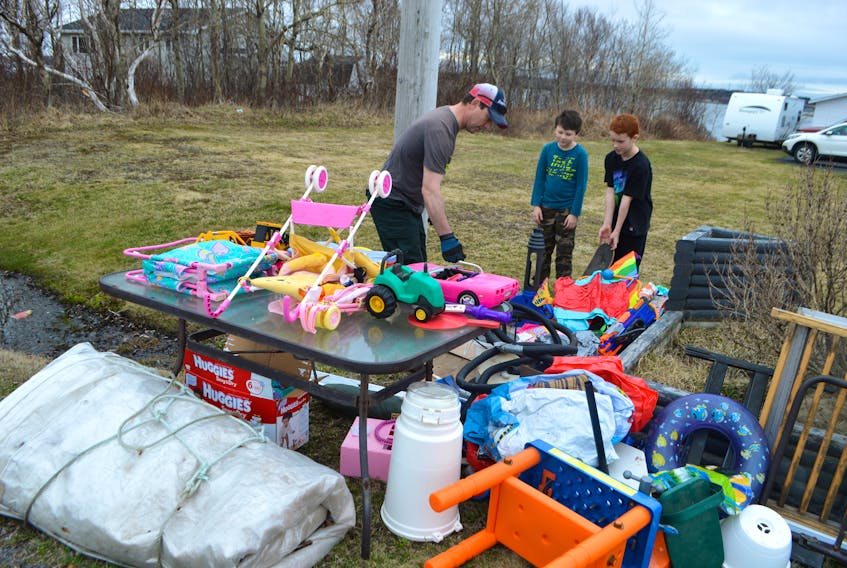 Scott Phillips, left, of Seaside Drive, Gardiner Mines, puts out items for heavy garbage assisted by family friend Ryan Coffin, centre, 7, and his son Matt Phillips, 10. The family set it up like a yard sale, making it easy for people to see what they had out. Scott said he put his first batch of heavy garbage out at 10 a.m. Monday and everything was gone by noon and he was in the process of putting a second load out. Phillips said he enjoys it, especially seeing children excited about toys they find, as well as chatting with people who stop by.