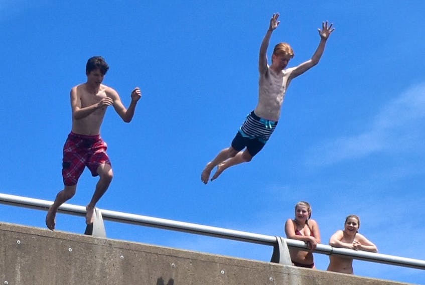 Glace Bay teens Nolan Parsons, left, and Evan McNeil soar off Albert Bridge and into the Mira River on Tuesday afternoon as a group of girls watch from above. The boys said there’s nothing better than a dip in the river when the weather is as hot and muggy as it was on Tuesday and is expected to be today.