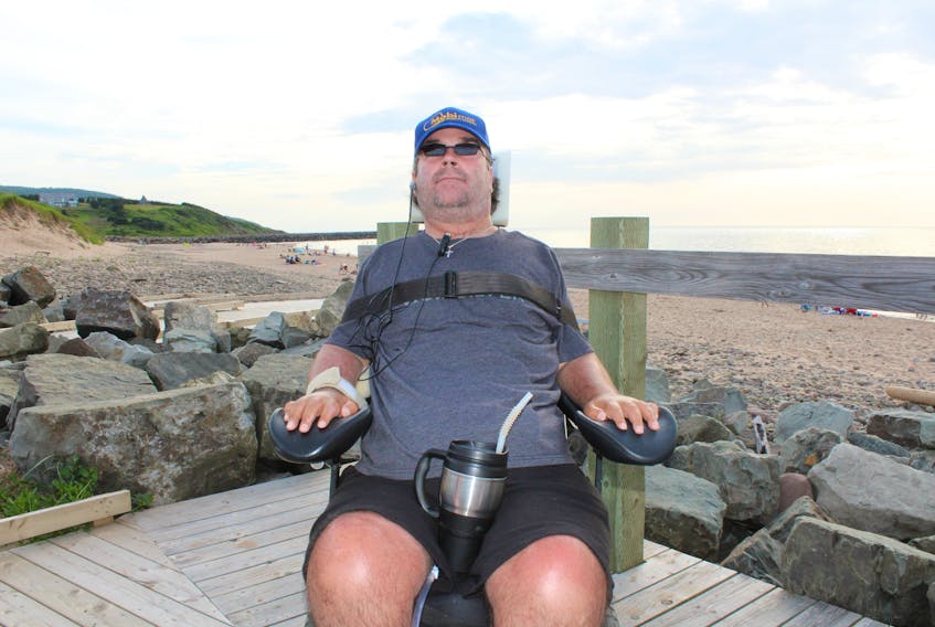 Callum MacQuarrie sits in his motorized wheelchair on the boardwalk at Inverness beach on Tuesday. In the background is the breakwater where he broke his neck diving into the shallow water below 23 years ago. MacQuarrie, who is co-chair of the Inverness County accessibility committee, helped lead the charge to make Inverness beach the most accessible beach in Atlantic Canada.