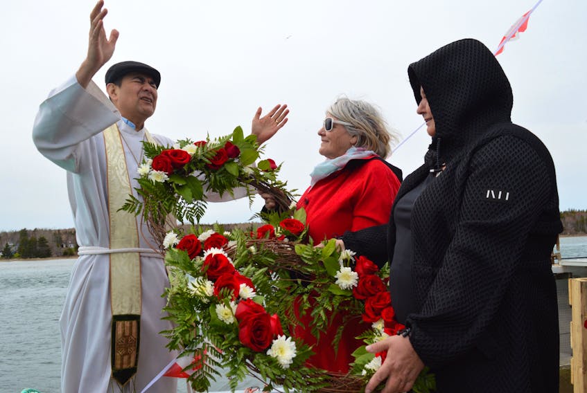 Rev. Julio Martin blesses a pair of rose-laden wreaths held by Mary R Marsh, centre, and Michelle Hawkins during the 64th annual Blessing of the Fleet at the government wharf in Alder Point. The women then tossed the wreaths into the water before a lengthy procession of people took turns throwing flowers into the ocean in memory of those lost at sea and of other loved ones who have passed. About 300 people attended the Alder Point gathering to mark the tradition that began in 1955.