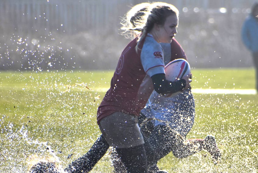 Sheridee Etheridge of the Riverview Rugrats carries the ball as her teammate falls in a puddle during the girls Highland region rugby championship game at Hub Field in Glace Bay last Wednesday. Field conditions weren’t ideal for the game, but that didn’t stop the Rugrats and Glace Bay Panthers boys team from capturing their respective league championships.
