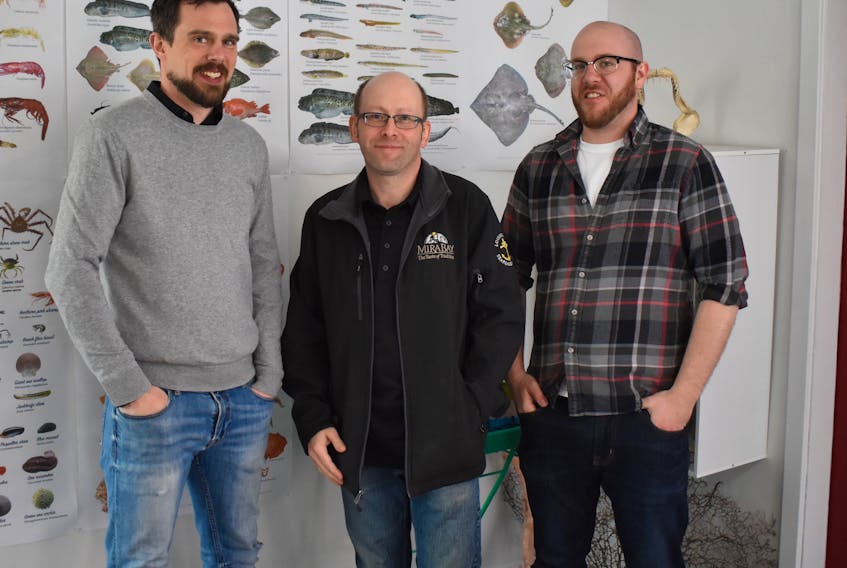 Eastern Nova Scotia Marine Stewardship Society members Adam Mugridge, Scott Samson and Kurt Simmons stand in front of a wall display at the new Oceans of Opportunity Marine Science and Heritage Centre in Louisbourg during its grand opening on Thursday.
