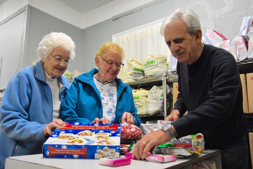 Constance Nickerson, left, Jean Landry and Lawrence Shebib look through different Christmas goodies in preparation for the Christmas Cheer dinner program. So far, the program has more than 200 people registered.