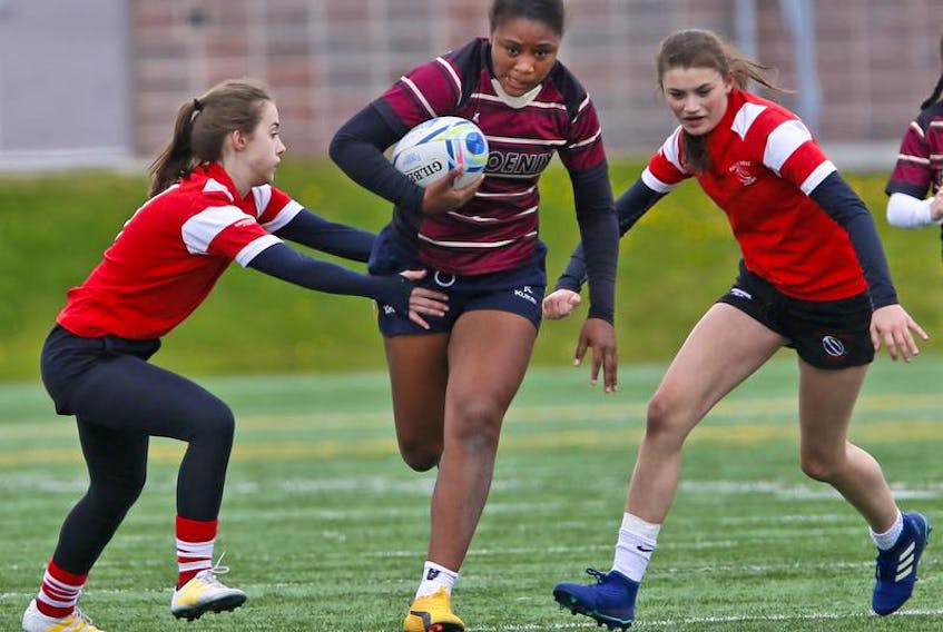 Citadel Phoenix’s Tashayla Tynes runs between a pair of Halifax West defenders during metro high school rugby action on the Mainland Common in Halifax.