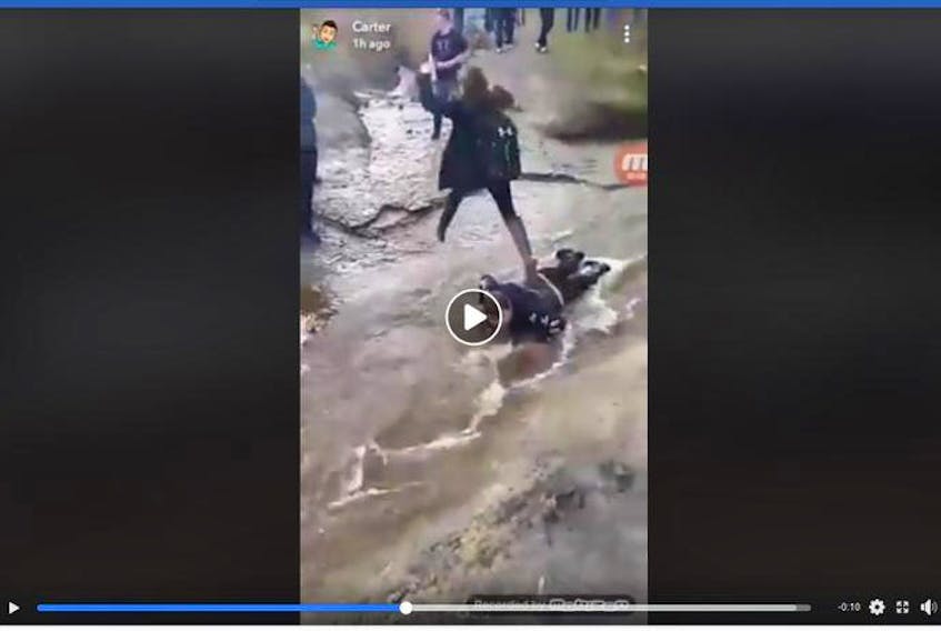 This Facebook video screen grab shows a teen laying in a stream and young girl waking on him.