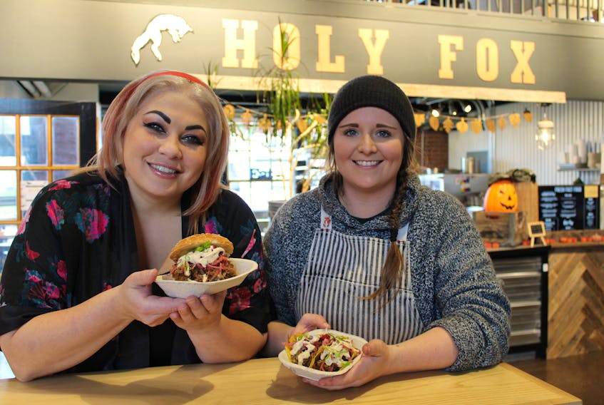 Chef Ilona Daniel, left, and chef Christine Dickey, co-owner of Holy Fox Food, show off Dickey’s braised pulled pork sandwich and tacos at Holy Fox’s location at Founders’ Hall Food Market in Charlottetown.