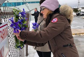 Lori Chynn of Deer Lake, whose husband John Pelley was lost in the Cougar Helicopters Flight 491 tragedy, places her tribute to him at the makeshift memorial on the chain-link fence outside the former Cougar Helicopters building at St. John’s International Airport this morning. Standing next to her is Julie Marsh of Torbay whose brother-in-law Corey Eddy of Sibley’s Cove, T.B., was also lost in the accident. Joe Gibbons/The Telegram