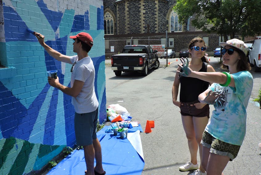 Altruistic Current's Amber Solberg describes her plans for a new mural now in progress to volunteer Lindy Decoste on Blowers Street on Saturday. The outdoor artwork will grace a passageway between buildings dubbed Penny Lane, after the Beatles song, and will be completed by the end of August.