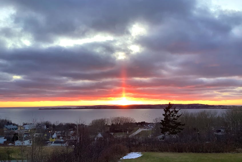 Yvonne MacDonald was at the right place at precisely the right time to capture this stunning sunset last Sunday evening.  Yvonne took the photo from her deck in Port Hood NS as the sun was lowering over Port Hood Island.  Yvonne says they get beautiful sunsets but she was surprised by the ray of red that was heading straight up to the amazing cloud formation. That shaft of light is called a sun or solar pillar. It’s created by the reflection of light from ice crystals. The hexagonal plate-like ice crystals fall with a horizontal orientation, gently rocking from side to side as they fall.