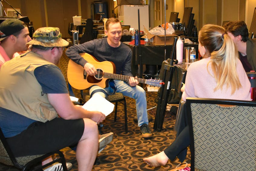 Mike Allison, the writer of We Are the Champions, teaching the cast harmonies from the gentle strum of his guitar.