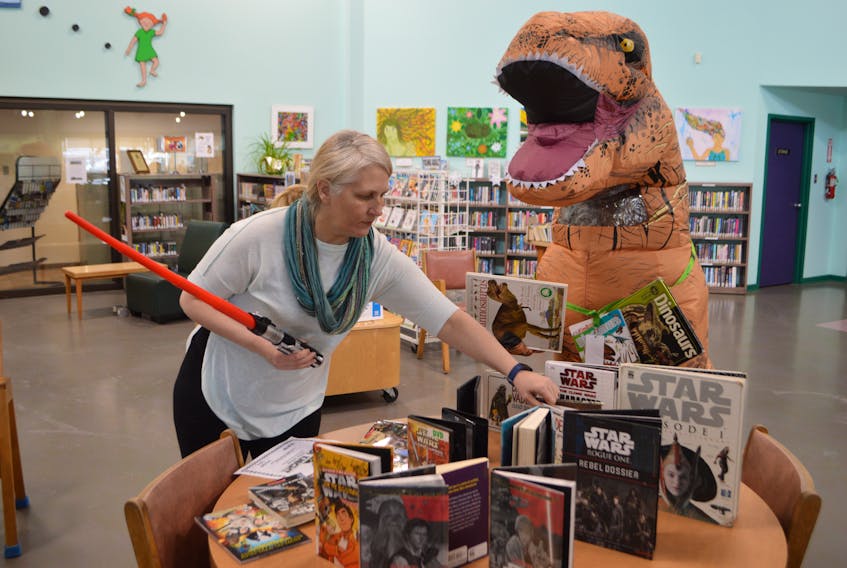Leslie MacPhee, library assistant at McConnell Library in Sydney, and Rexie the Tyrannosaurus rex, prepare for an upcoming Super Saturday at the library. This week's Saturday fun day, which is open to all ages, will feature Star Wars from 10 a.m.-2 p.m., sponsored by the credit union, and the Jan. 25 event will be Family Literacy Dinosaur Day from 10 a.m.-4 p.m. Star Wars Day will include a Jedi training room, crafts, a chance to win a mystery prize by checking out a book, and much more. Family Literacy Day on Jan. 25 will feature the dinosaur era. All library programs are free of charge. Sharon Montgomery-Dupe/Cape Breton Post