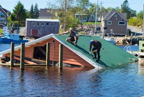 A couple of men work on dismantling a metal roof from a boathouse in Herring Cove that was blown into the water during Dorian.