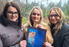 Nadea Melenchuk, Leah Profitt and Lacey Conrad (from left) hold a print of a poster promoting a campaign to bring kindness to others as a way of marking what would have been their mother's 60th birthday. Leslie Ann Conrad was murdered 14 years ago in Kings County.
