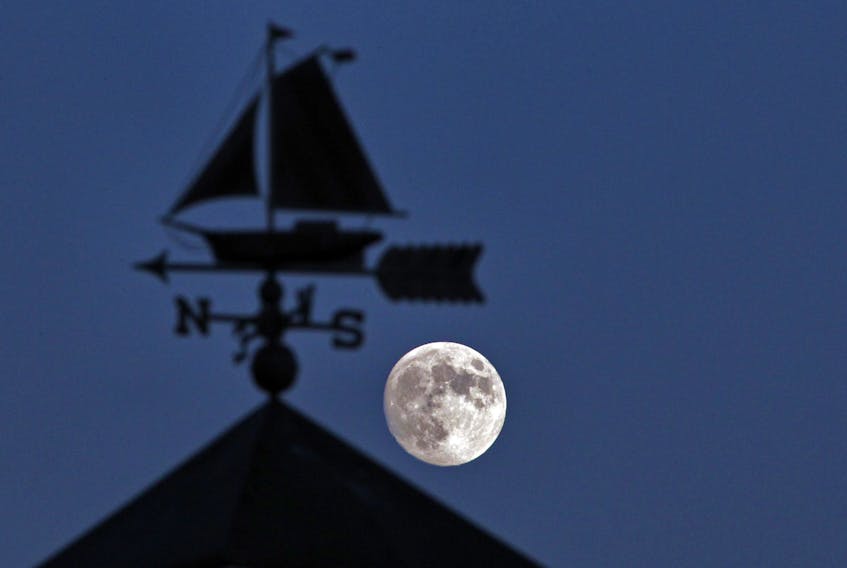 An approaching full moon (two days away) is framed by a weather vane atop the cupola on a gift shop in Eastern Passage, in this 2012 file photo.