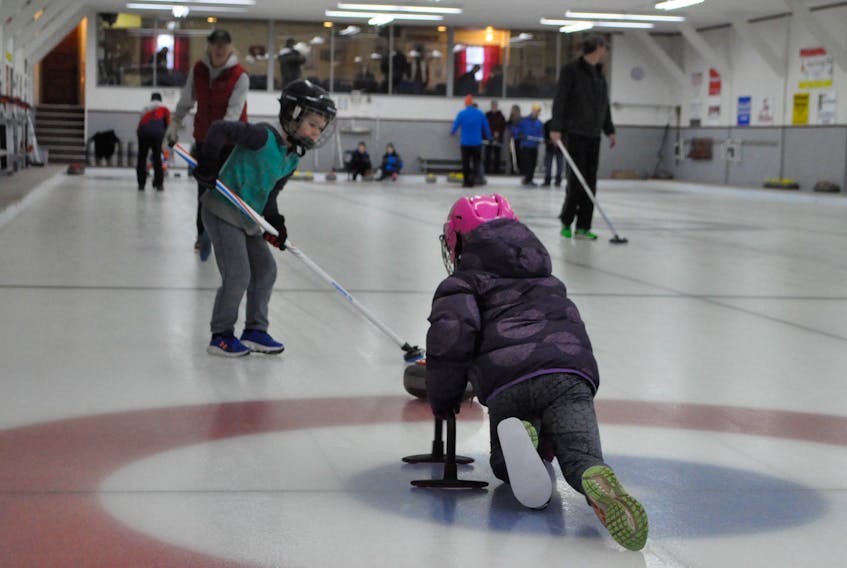 Payton Roles, 7, throws the rock to her brother, Grady, 6, who gets ready to sweep it down the ice.