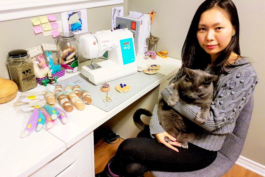 Jenna Park holds her cat, the Grey Gatsby, at her desk, where she creates her handmade cat toys.