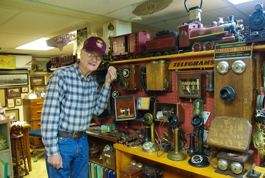 Tony Kalkman checks some of the old railway telephones that are in his collection.  On the shelf above is a miniature steam locomotive and miniature cars, duplicates of the railway stock that once ran up and down local rails. The miniatures were made from scrap material.