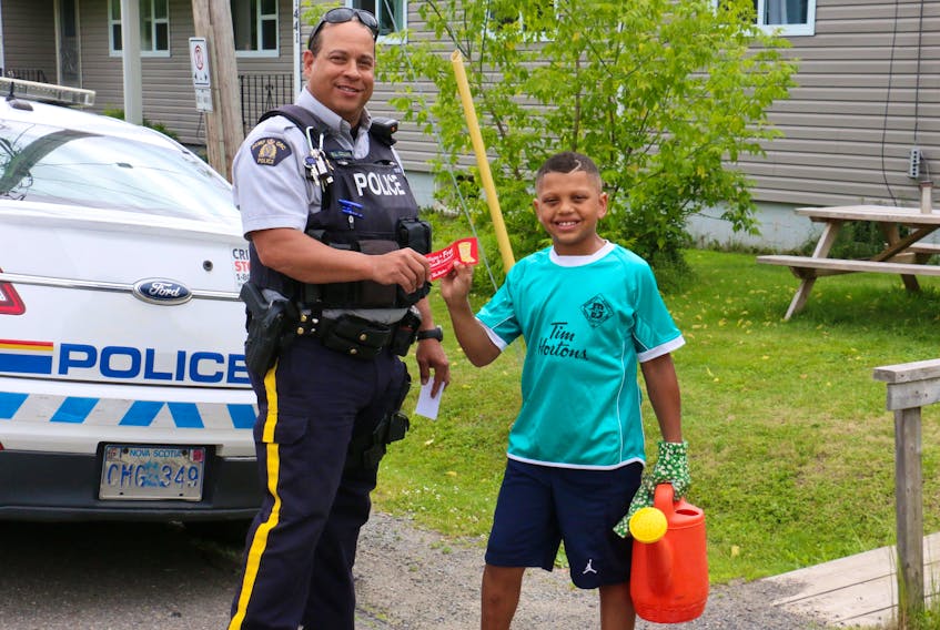 Const. Richard Collins, of the Windsor rural RCMP detachment, presents nine-year-old Rayez Sampson, of Curry's Corner, with a reward for being caught doing something that benefited his neighbour.