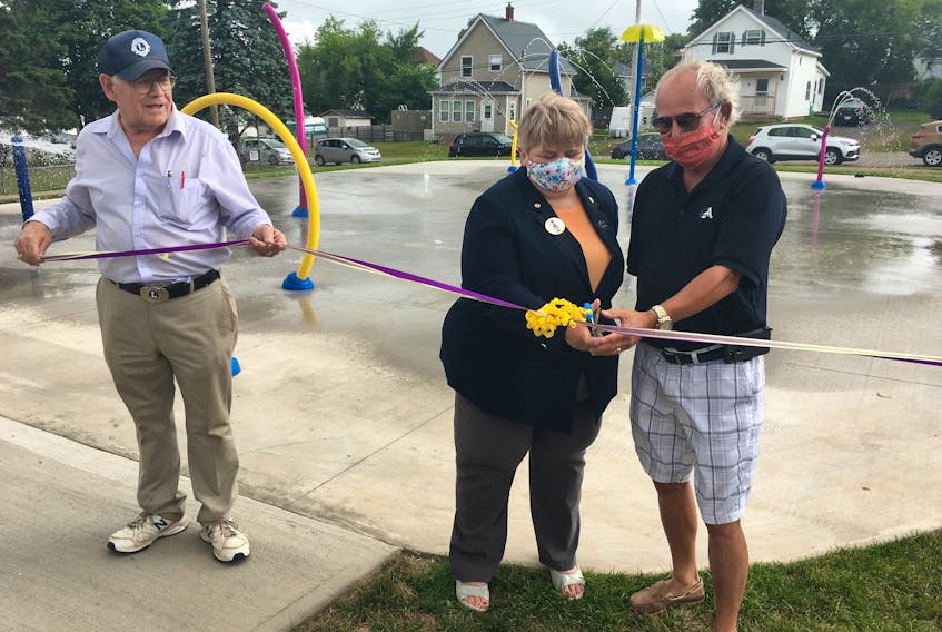 Amherst Lions Club park committee chairman Rubin Millard (left) looks on as Lions District Governor Jane Gregory and Amherst Mayor David Kogon cut the ribbon to officially open a $165,000 splash pad at the Lions Park in Amherst.