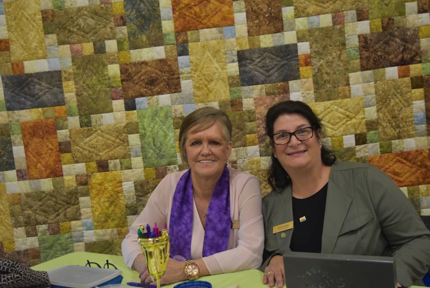 Debra Battist and Wanita Atkins together at a table selling tickets for the Stepping Stones quilt which was a guild group project.