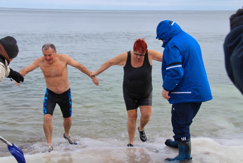 Bill MacEachern, left, helps a fellow swimmer out of the waters at Melmerby Beach following a polar bear swim Monday morning. This was MacEachern’s 19th consecutive year taking part in such a swim.