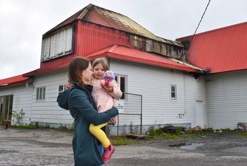 Carly Wynn-Baudoux and her daughter Ruby look at the building in which they were renovating the upstairs as their family home. Ruby holds a stuffed animal given to her by a firefighter.