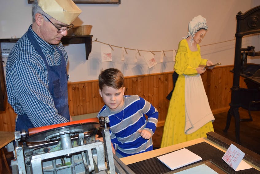 Cameron Horton had the opportunity to learn how to make a Christmas card with a printing press during a visit to the Museum of Industry in Stellarton on Friday. Pictured showing him how to use the press is education curator Andrew Phillips.