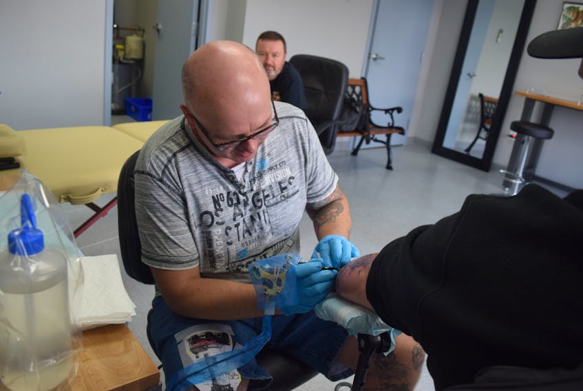 Danny Hay etches some new ink onto a customer at The Tattoo Place, a new tattoo parlour that opened on East River Road, as his fellow co-owner Mike LeBlanc looks on.