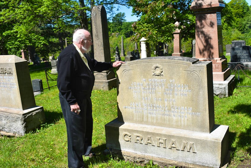 William Graham stands beside his grandfather’s headstone in the Riverside Cemetery.