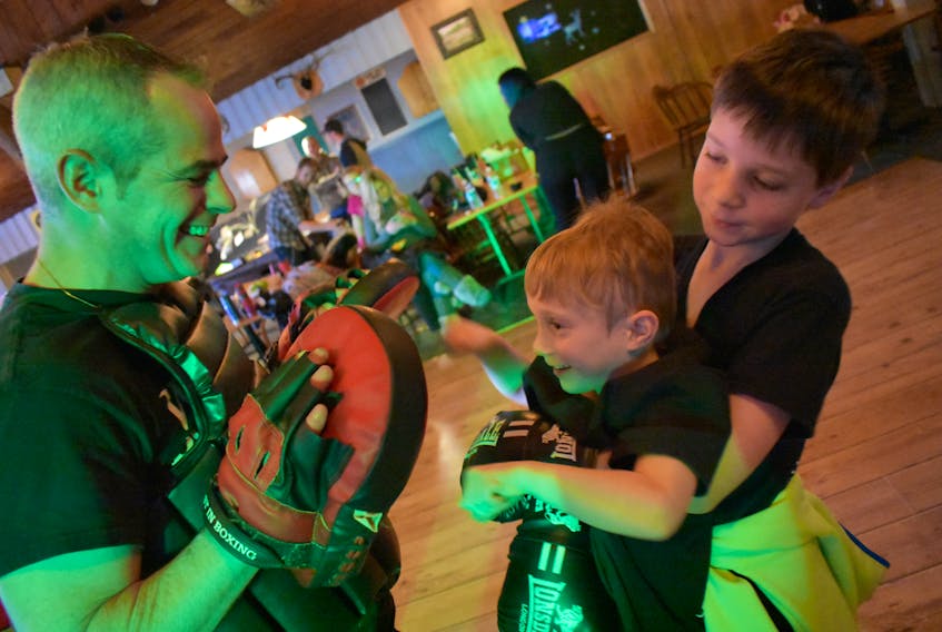 Kieran Raisbeck (right) holds up his little buddy Logan Bradley to take a few punches with coach Aaron Kinch at Westville’s White Tail Pub Saturday. All three were trading punches as part of Westville Boxing Club’s first annual fundraiser.
