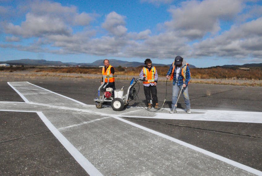 Despite PAL Airlines announcing it is pulling out of Stephenville airport in mid-January, it was business as usual at the airport Thursday as workers with Precision Enterprises were painting lines on the main runway and large Xs on the cross runway. Airport security official Bruce Kinslow, left, looks on as Pheabie Rumbolt and Patrick Lannon carry out the painting. FRANK GALE/ THE WESTERN STAR
