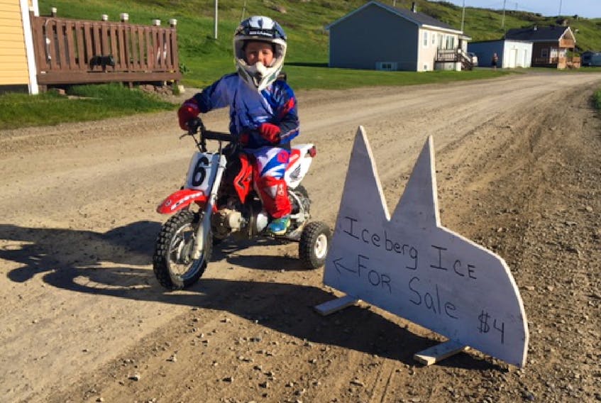 Jax Ryland, six, of L’Anse Amour on his hard-earned dirt bike next to the sign for his iceberg ice business. - Photo courtesy of Lisa Davis-Ryland