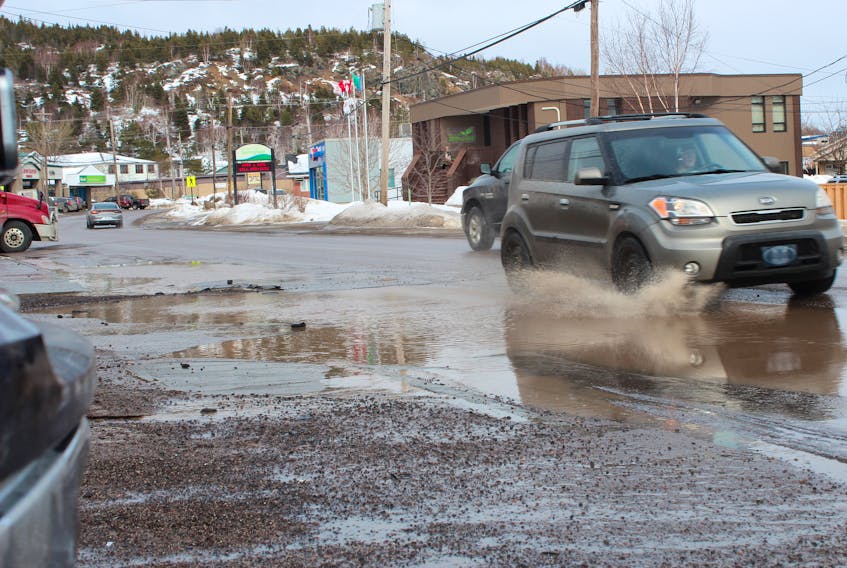 Motorists attempt to maneuver a large water-filled pothole on Springdale’s Main Street. The mayor says the town’s efforts to stay on top of poor road conditions have been futile.
