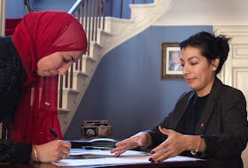 Haidi El Mefary signs herself into Canadian citizenship as Milargos Barrueto, application processing agent for Immigration, Refugees and Citizenship Canada, looks on. - Ernesto Carranza