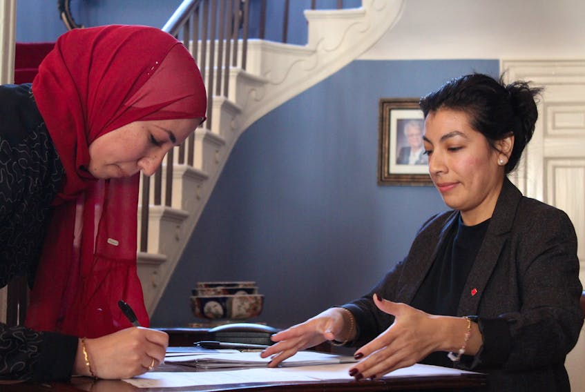Haidi El Mefary signs herself into Canadian citizenship as Milargos Barrueto, application processing agent for Immigration, Refugees and Citizenship Canada, looks on. - Ernesto Carranza