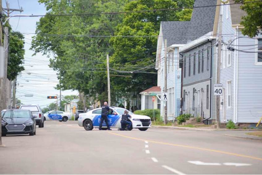 Charlottetown police officers take cover behind a cruiser on Euston Street during a standoff with a man inside a nearby building on Friday.