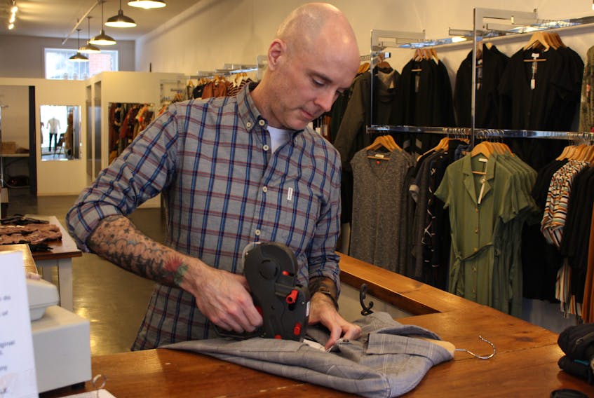 Owner Joe Millar prices a shirt in Colourblind Boutique. Millar reduces prices regularly or donates items to avoid clothing waste common in the retail clothing industry.