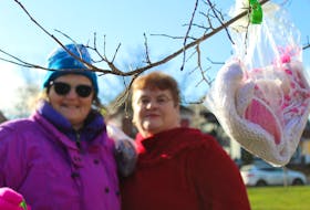 Ella Wall, left, and Betty Begg-Brooks hang bags containing winter gear from some trees at Hillsborough Square in Charlottetown this past weekend. The bags, which include items like gloves, toques and scarves, are available for whoever may need them on a cold winter day. Daniel Brown/The Guardian.