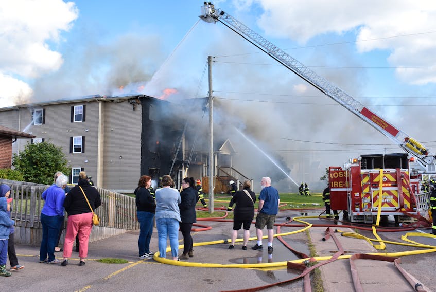 Residents and onlookers stand in the parking lot next door to the Glen Stewart Drive apartment building as fire fighters douse the building with water on Saturday afternoon.