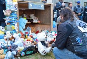 A member of Guardians of the Children, a motorcycle group that advocates for families, places a teddy bear at the memorial for Knox Whitlock, a two-year-old Summerside boy who died last week.