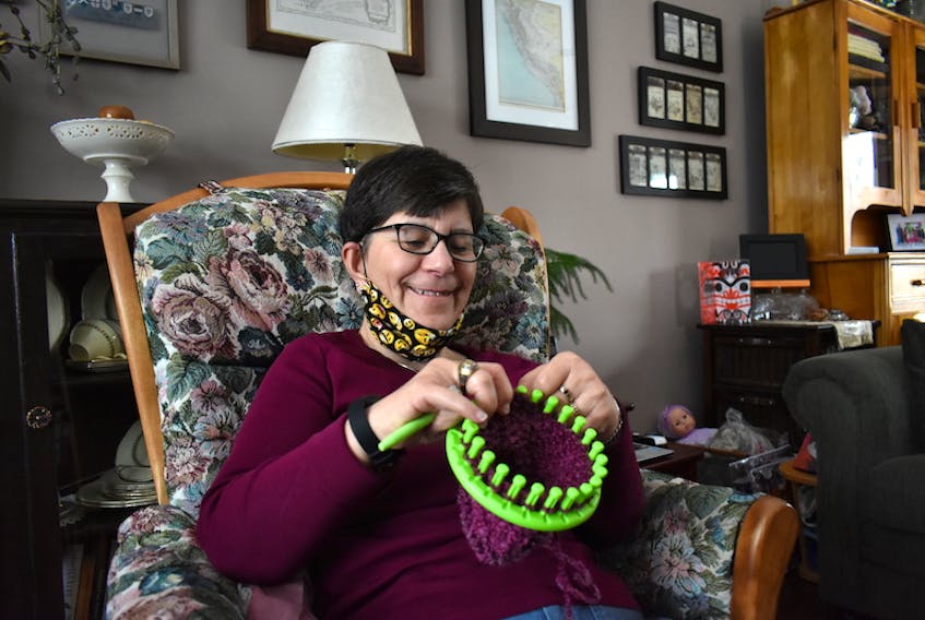 Monique Gauthier smiles while working on a baby cap in her living room. She sits in this chair almost every day to work on the knitted hats she donates.